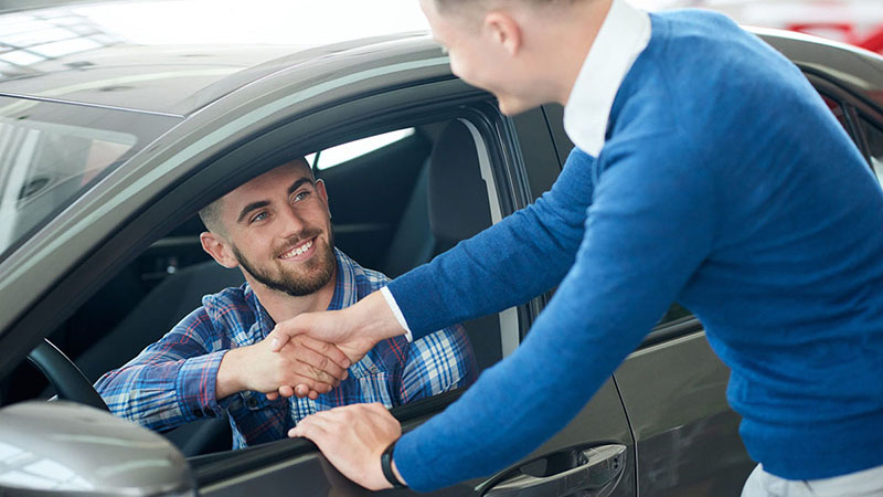 smiling customer in car shaking hands with sales professional